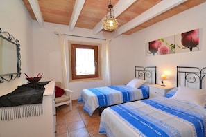 A bedroom with two beds, a desk, a chair, a window, and a ceiling light fixture.