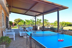An outdoor ping pong table with a net, surrounded by white chairs and a covered seating area.
