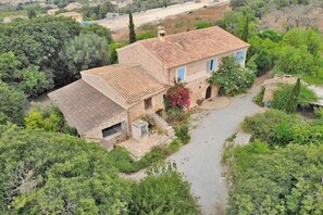 Ein Haus aus Stein mit einem Ziegeldach, umgeben von viel Grün und einer gepflasterten Auffahrt.