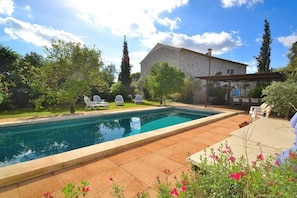A swimming pool with a stone building in the background, surrounded by greenery and outdoor seating. - Finca in Llubi with swimming pool (Llubi)