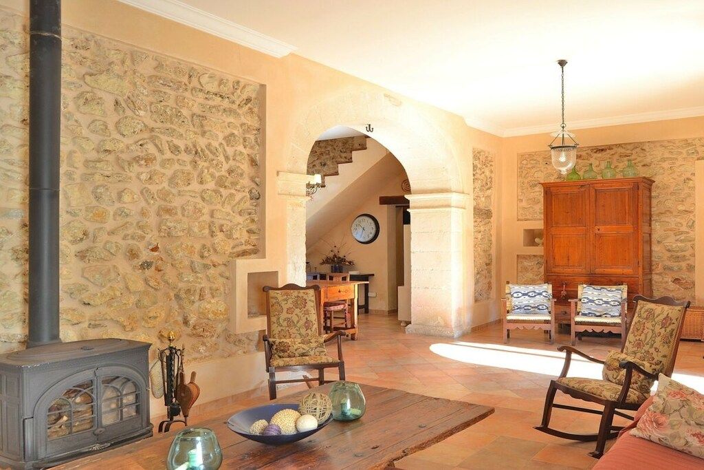 A cozy living room with a stone wall, a fireplace, a wooden table with decorative items, and a wooden cabinet.