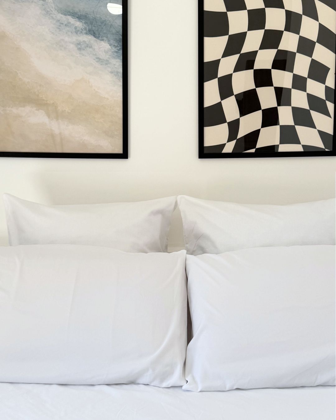 Una cama con ropa de cama blanca y dos cuadros enmarcados encima.