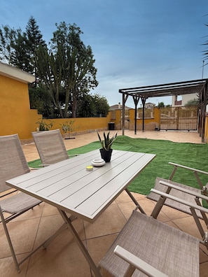 Eine Terrasse mit Tisch und Stühlen, einem Blumentopf und einer Pergola.