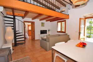 A spacious living area with a staircase, a television, a sofa, and a dining table with fruit.
