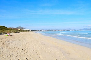 A wide sandy beach with footprints, a clear sky, and distant mountains.