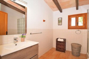A bathroom with a white sink, wooden vanity, a mirror, a small potted plant, a wicker basket, and a window with wooden shutters.