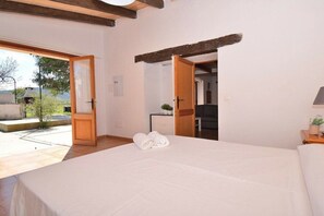 A bedroom with a large bed, a wooden door leading to a balcony, and a view of the outdoors.