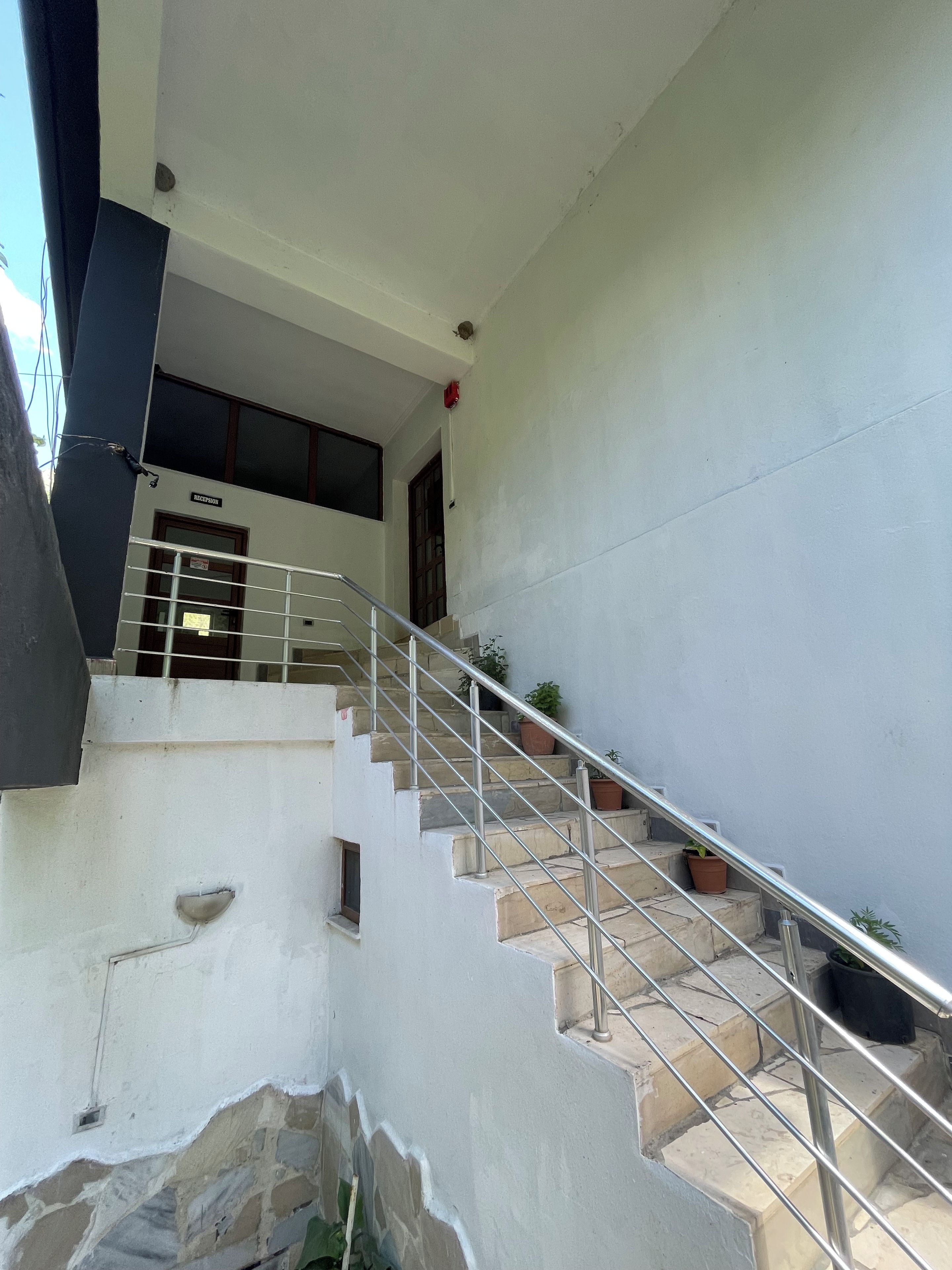 Una escalera con barandillas metálicas que conduce a un rellano con una puerta que indica 'RECEPTION'.