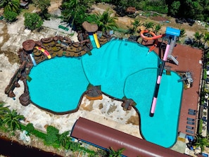 Uma grande piscina ao ar livre com uma cascata, cercada por palmeiras e um deck de madeira.
