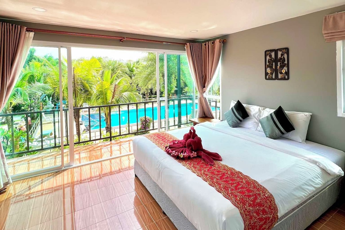 Quarto de hotel com uma cama grande, vista para uma piscina e varanda.
