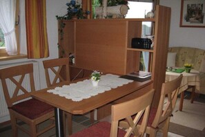 Ein Essbereich mit einem Holztisch, Stühlen, einer Spitzenleinentischdecke und einem kleinen Blumentopf.