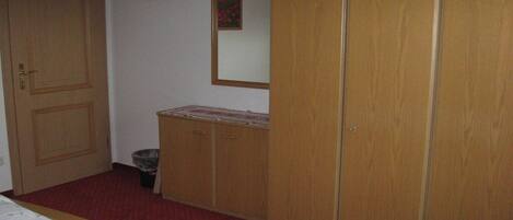 Une chambre à coucher avec un lit, une armoire en bois et une petite poubelle.