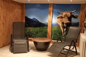 A room with a large wall mural of a cow, a foldable chair, a small table, and wooden paneling. - Eldorado Holiday Apartment Dream Dancer (Bolsterlang)