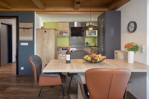 A modern kitchen with a dining area, wooden cabinets, a built-in oven, and a fruit bowl on the table. - Eldorado Holiday Apartment Dream Dancer (Bolsterlang)