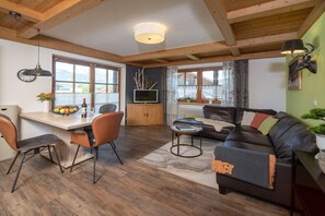 A cozy living area with a sofa, a dining table with chairs, a television, and a fireplace. - Eldorado Holiday Apartment Dream Dancer (Bolsterlang)