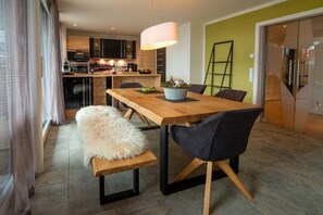 A modern dining area with a wooden table, black chairs, and a fluffy white bench. - Holiday apartment with 3 bedrooms (Bolsterlang)