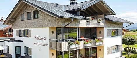 Une maison à deux étages dotée d’un balcon, d’une terrasse couverte et d’une pelouse bien entretenue.