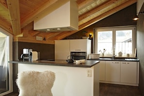Een keuken met een houten plafond, witte kastjes, een aanrecht en een raam met uitzicht.