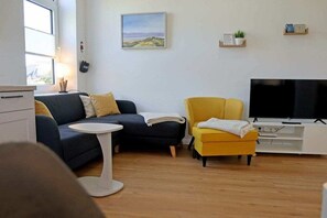 A modern living room with a sofa, armchair, TV, and a small table. - Holiday apartment with 1 bedroom (Dollerup)
