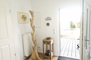 Een kamer met een houten sculptuur, een klein houten tafeltje met een schaal, en een deur naar buiten.