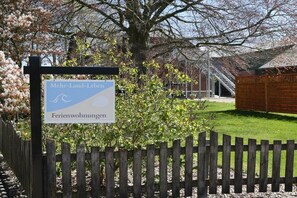 A sign with text in a foreign language, a wooden fence, and a building in the background. - Holiday apartment with 1 bedroom (Dollerup)