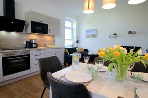 Een moderne keuken met witte kastjes, een magnetron en een oven. Er staat een eettafel gedekt met borden, glazen en een bloevas.