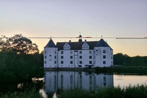 A large, white building with multiple towers, situated by a calm body of water, reflecting the structure. - Holiday apartment with 1 bedroom (Dollerup)