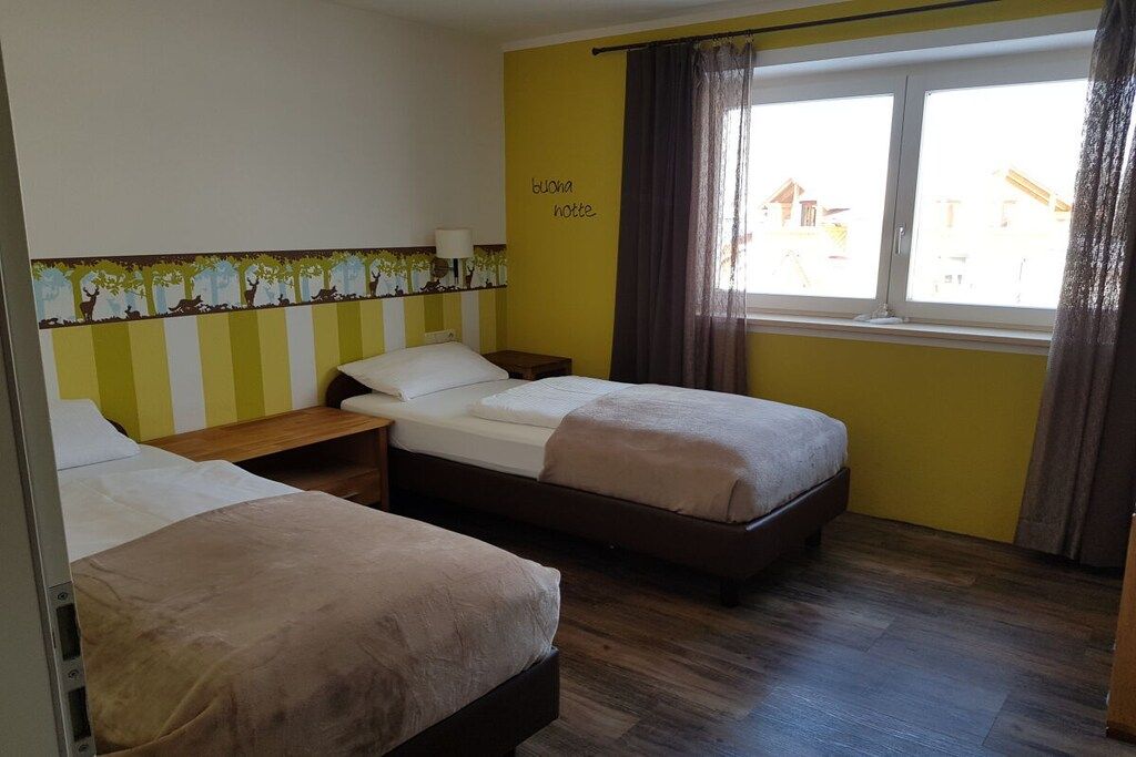 Ein Hotelzimmer mit zwei Betten, einem fensterbelaubten Fenster und einer Wand mit Baumdekor.