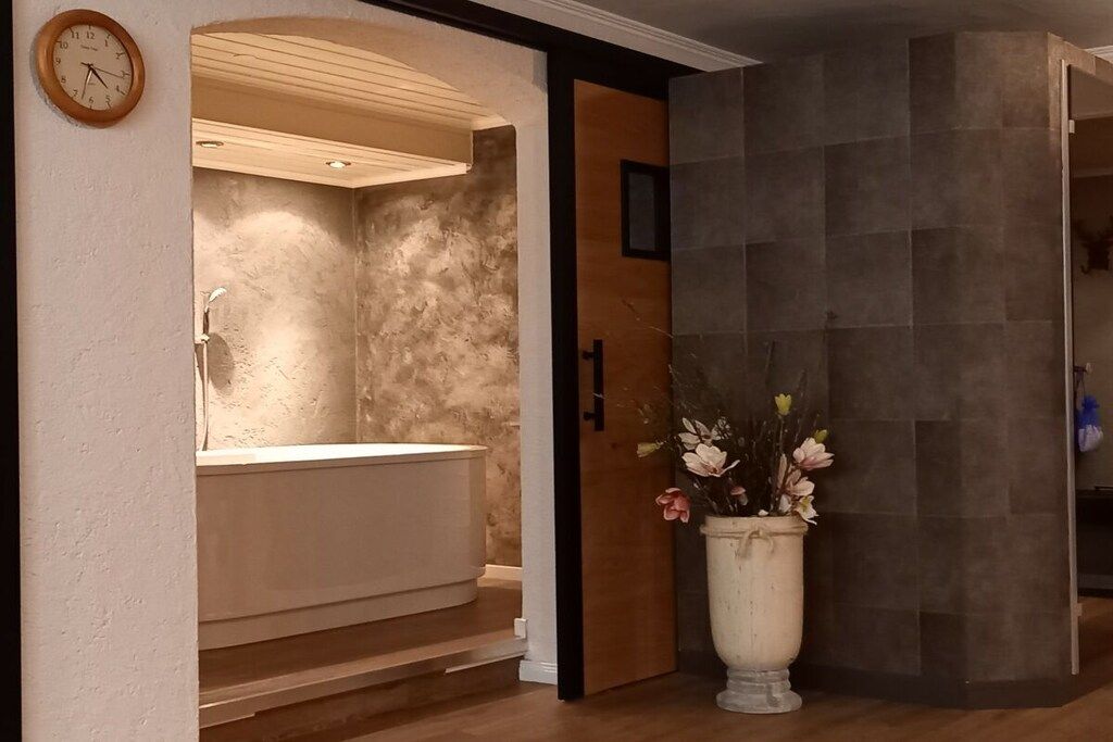 A bathroom with a bathtub, a wooden door, and a potted plant.