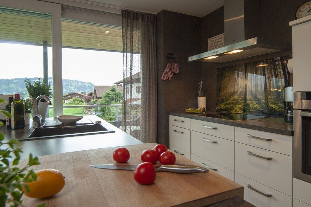 A modern kitchen with a large window, a cutting board with tomatoes, and a knife.