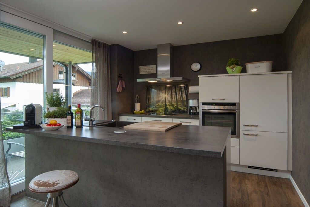 A modern kitchen with a large island, built-in oven, and a view of the outside.