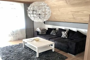Una sala de estar moderna con una mesa de centro blanca, un sofá negro con cojines estampados y una lámpara esférica original.