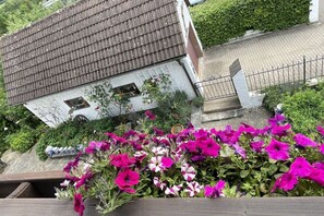 Et hus med skrå tag, et lille vindue og en have med blomstrende blomster.