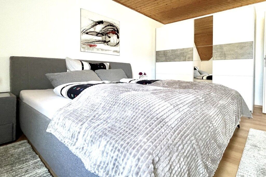 A modern bedroom with a large bed, a grey headboard, and a painting on the wall.