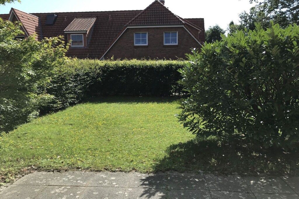 A residential property with a well-maintained lawn, a brick house with a tiled roof, and a hedge in the foreground.