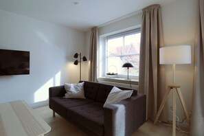 Ein modernes Wohnzimmer mit einem dunkelbraunen Sofa, einem weißen Sessel, einer Stehlampe und einem Tisch.