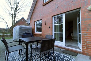 Eine Terrasse mit Tisch und Stühlen, ein überdachtes Objekt sowie ein Haus mit Backsteinfassade und einer Schiebetür.