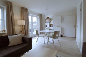 Ein modernes Wohnzimmer mit einer Couch, einem Esstisch mit Stühlen, einer Lampe und einer Küchenzeile im Hintergrund.