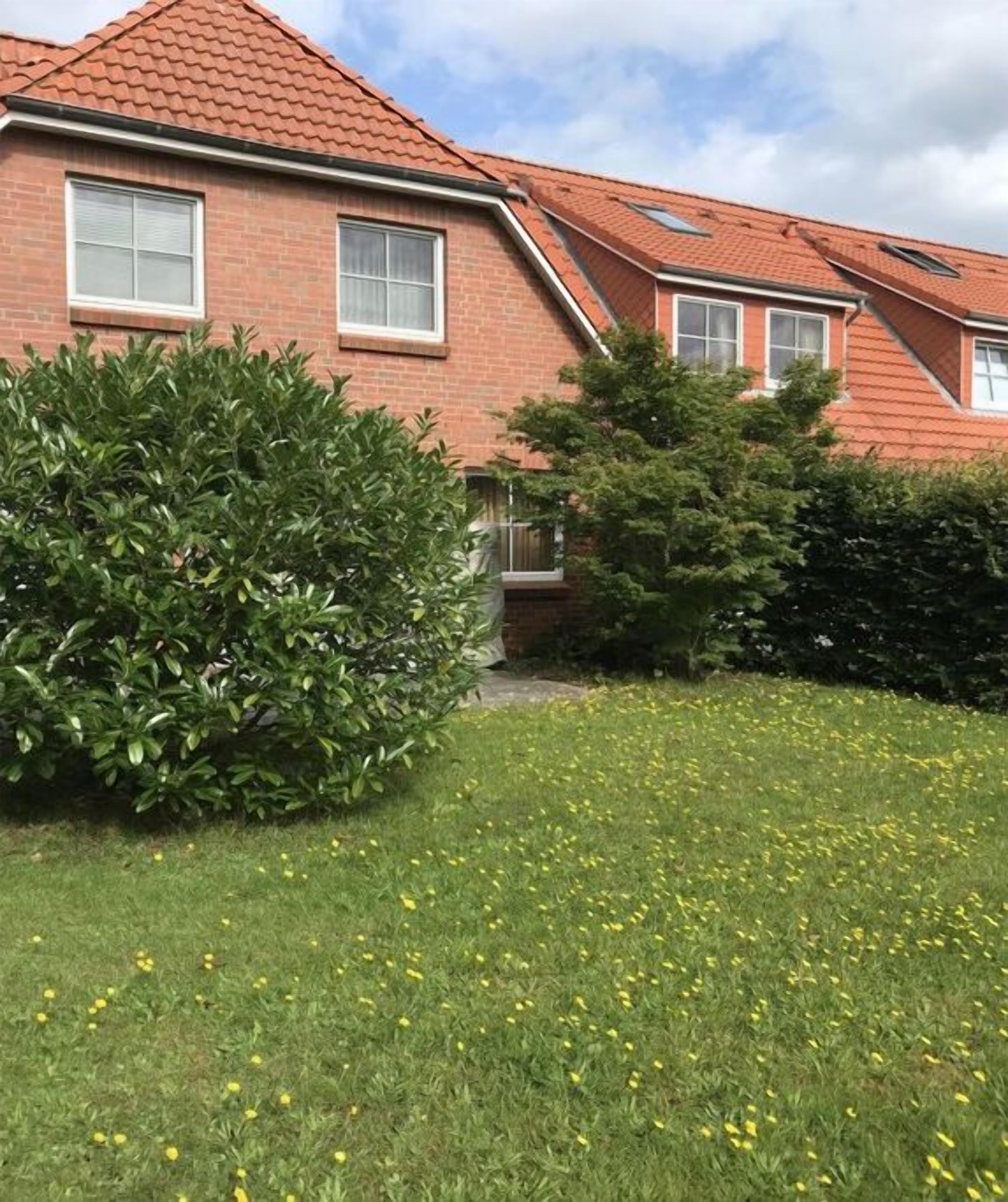 A residential building with a red-tiled roof, a brick facade, and a well-maintained lawn with yellow flowers.