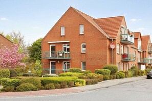 Ein rotes Mehrfamilienhaus mit Balkon, kleinem Garten und blauem Himmel.