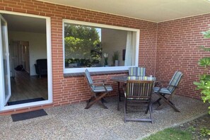 Een terras met een bakstenen muur, een schuifpui en een tafel met vier stoelen.