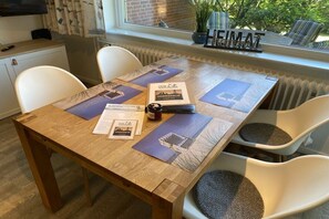 Een houten eettafel met vier stoelen, een raam met uitzicht op groen, en een bordje met de tekst 'HEIMAT' op de vensterbank.