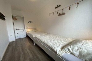 Een kamer met een enkel bed, een kledingkast, een nachtkastje en een wandlamp.
