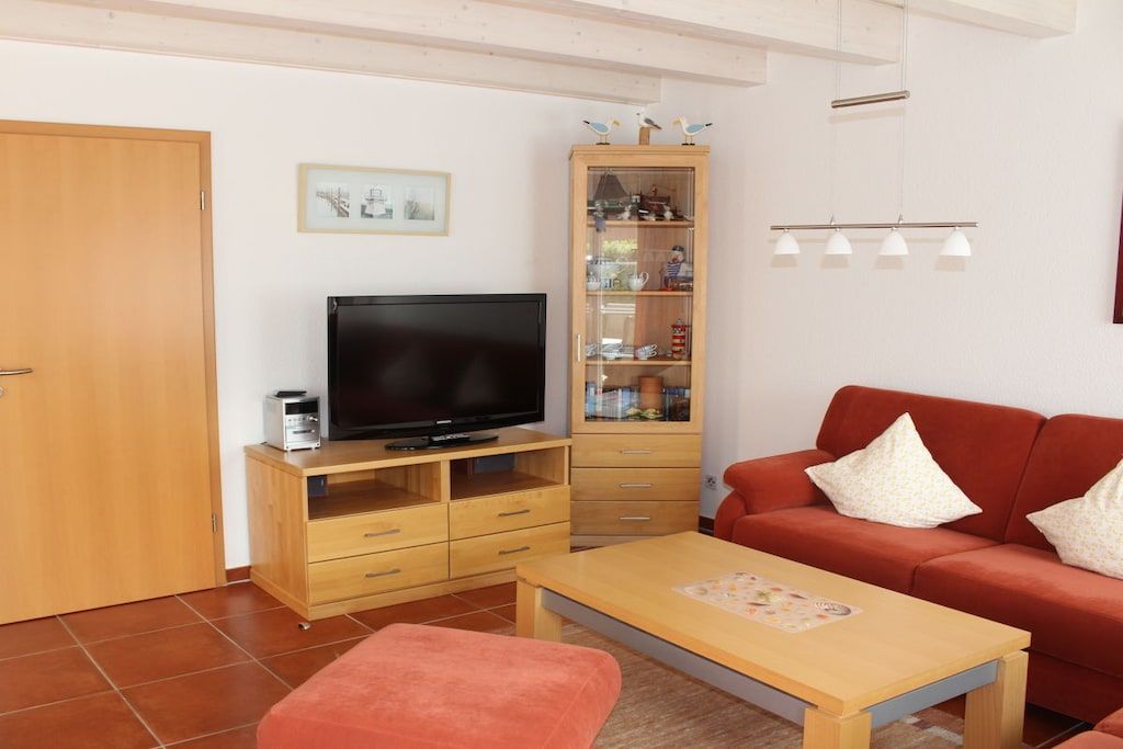 A living room with a television on a wooden cabinet, a red sofa, a wooden coffee table, and a cabinet with glass doors.
