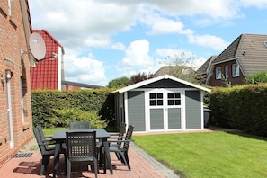 A brick building with a satellite dish, a small shed with a door, and a table with chairs in the foreground. - Holiday home with 3 bedrooms (Greetsiel)