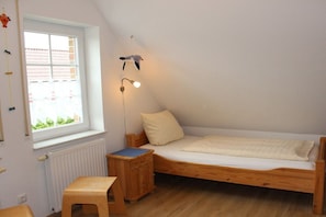 A small, single-bed room with a sloped ceiling, a window, a bedside table, and a nightstand. - Holiday home with 3 bedrooms (Greetsiel)