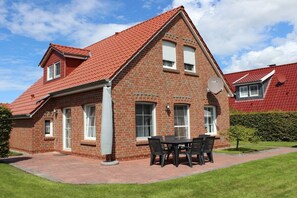 Ein Ziegelhaus mit rotem Dach, einer Terrasse mit Tisch und Stühlen sowie einem gepflegten Rasen.
