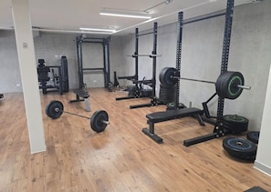 A gym with weightlifting equipment, benches, and a wooden floor. - Luxury Condo with Spectacular Ocean Views—oceanfront, pools, gym, rooftop (Jacó)