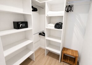 A walk-in closet with open shelves, a small wooden stool, and a black electronic device. - Luxury Condo with Spectacular Ocean Views—oceanfront, pools, gym, rooftop (Jacó)