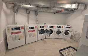 A laundry facility with multiple washing machines and dryers, ventilation ducts, and a tiled floor. - Luxury apartment with spectacular ocean views—right on the water, with pools, a fitness center, and a rooftop terrace (Jacó)